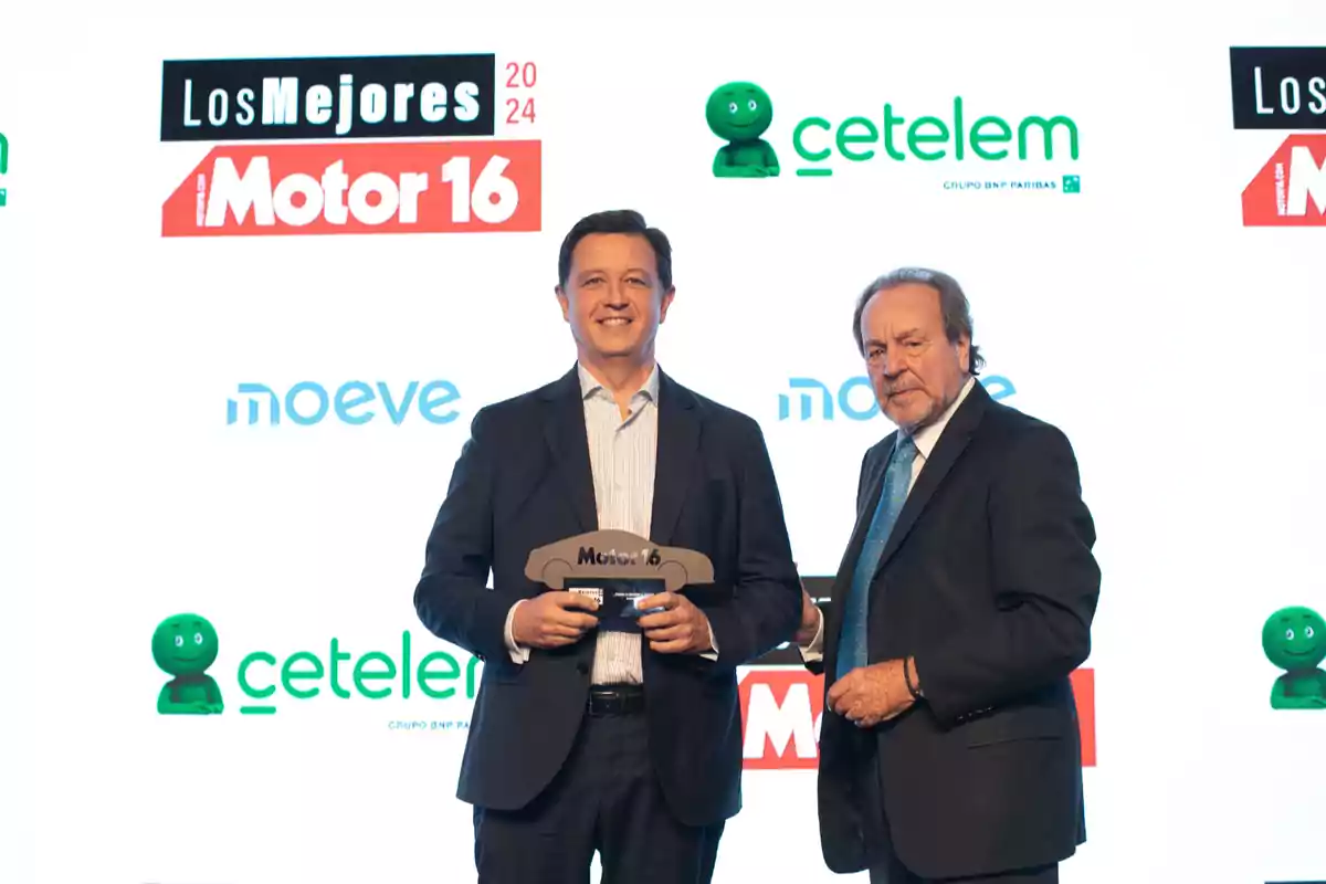 Dos hombres en traje posan con un trofeo en un evento de premios, con logotipos de Motor 16 y Cetelem en el fondo.