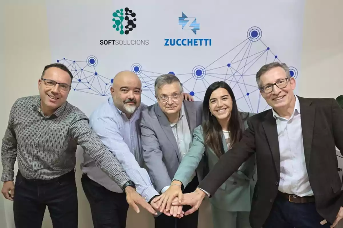 Cinco personas posan juntas con las manos unidas frente a un fondo con logotipos de Softsolucions y Zucchetti.