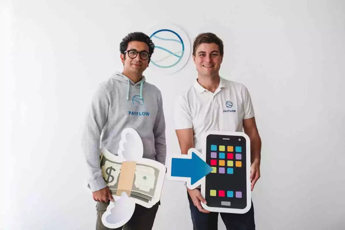 Dos hombres sonrientes con camisetas de Payflow sostienen figuras de billetes con alas y un teléfono móvil frente a un fondo blanco con el logo de la empresa
