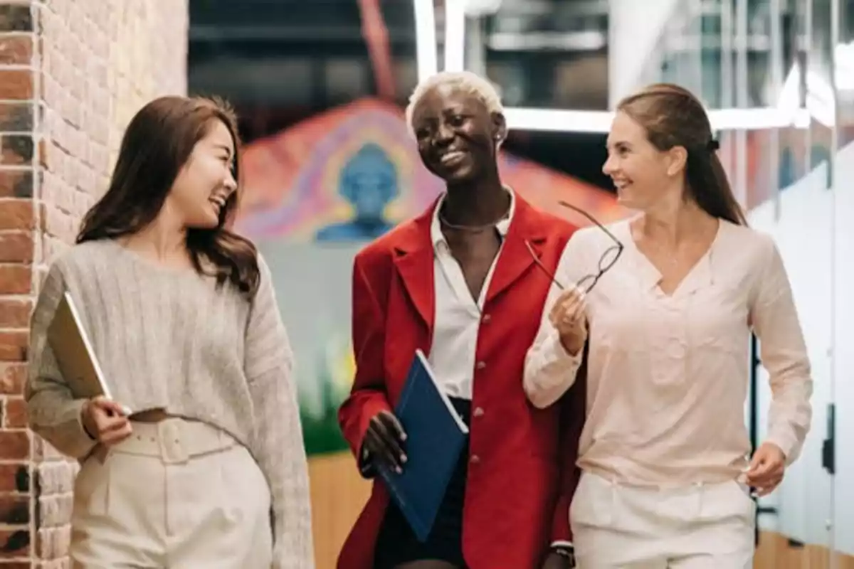 Tres mujeres caminando y sonriendo en un entorno de oficina.