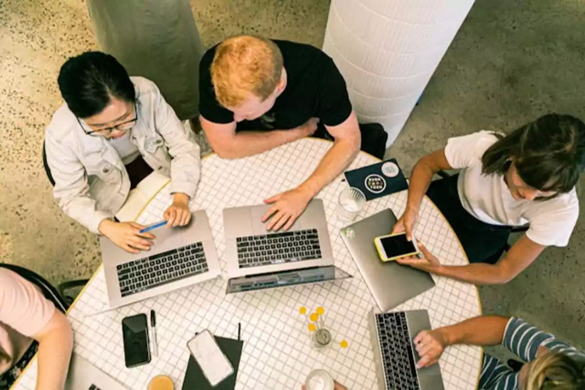 Personas trabajando en una mesa con computadoras portátiles y teléfonos móviles.