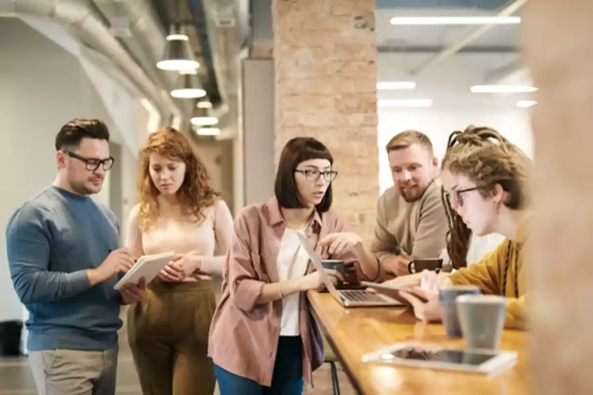 Un grupo de personas trabajando y colaborando en una oficina moderna con laptops y tabletas.