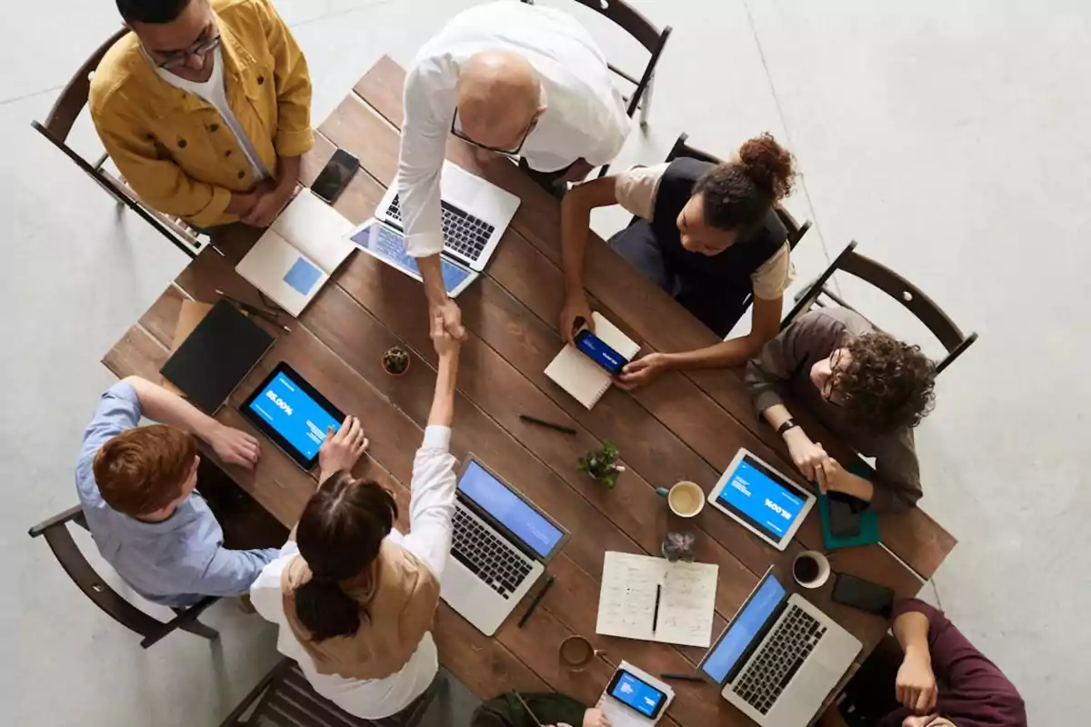 Un grupo de personas trabajando en equipo alrededor de una mesa con computadoras portátiles y tabletas.