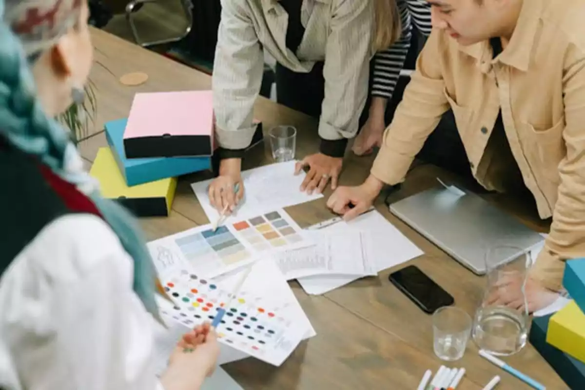 Personas trabajando en un proyecto de diseño con muestras de colores y documentos sobre una mesa.