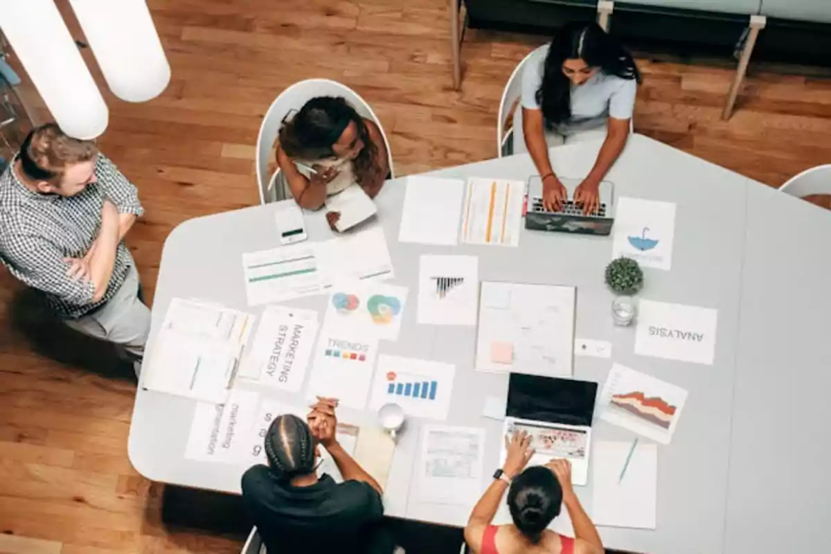 Un grupo de personas trabajando en una mesa con documentos y laptops.