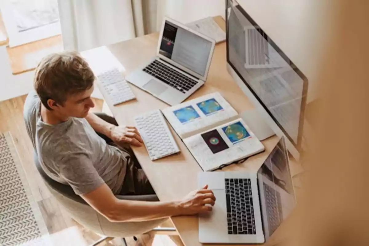 Persona trabajando en un escritorio con múltiples computadoras portátiles y monitores.