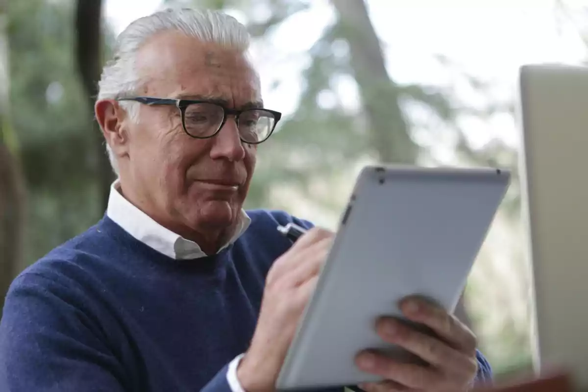 Hombre mayor con gafas usando una tableta digital en un entorno al aire libre.