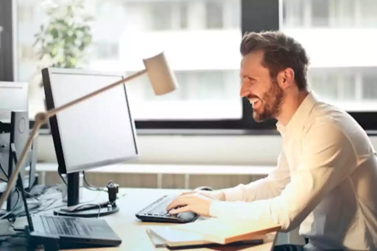 Hombre sonriendo mientras trabaja en una computadora en una oficina moderna.