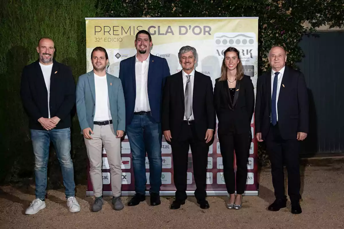 Un grupo de seis personas posando frente a un cartel en un evento formal.