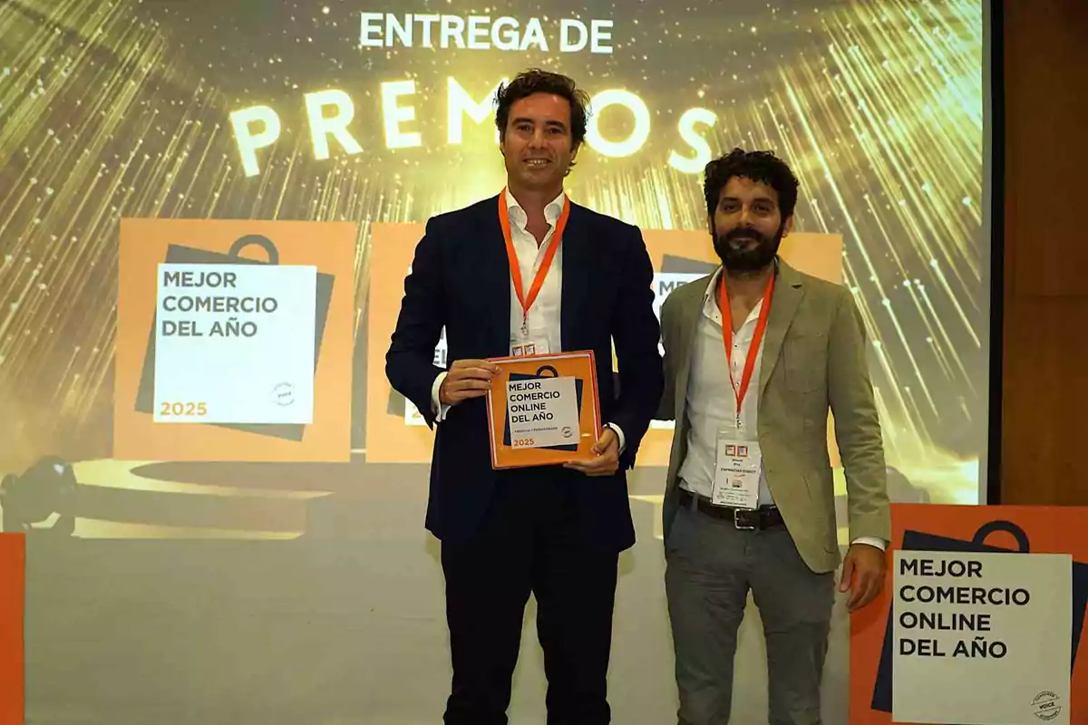 Dos hombres posan en un evento de entrega de premios, uno de ellos sostiene un reconocimiento al "Mejor Comercio Online del Año 2025".