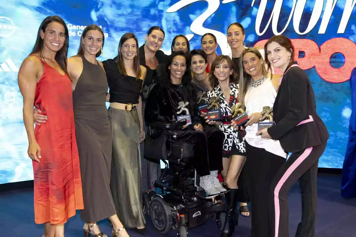 Un grupo de mujeres sonrientes posando para una foto, algunas de ellas sosteniendo trofeos, con un fondo azul que tiene texto blanco y rojo.