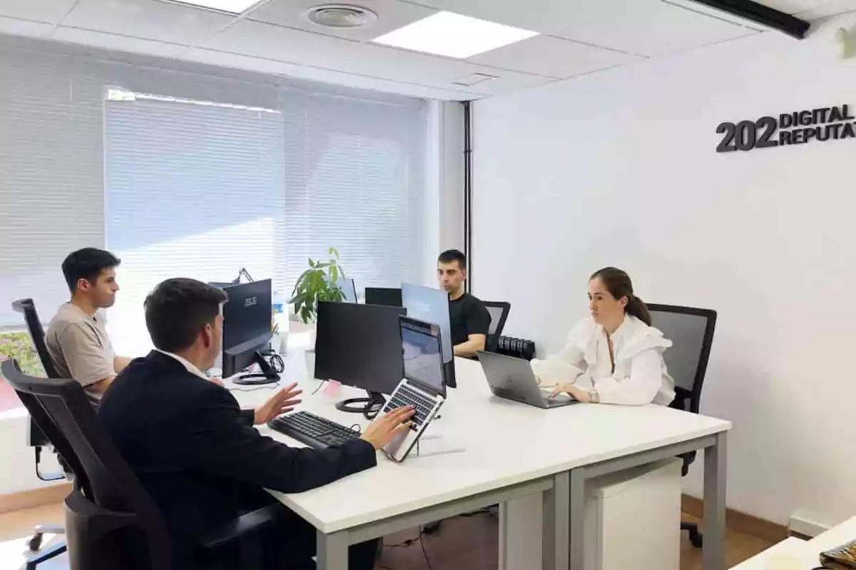 Un grupo de personas trabajando en una oficina moderna con computadoras y laptops.