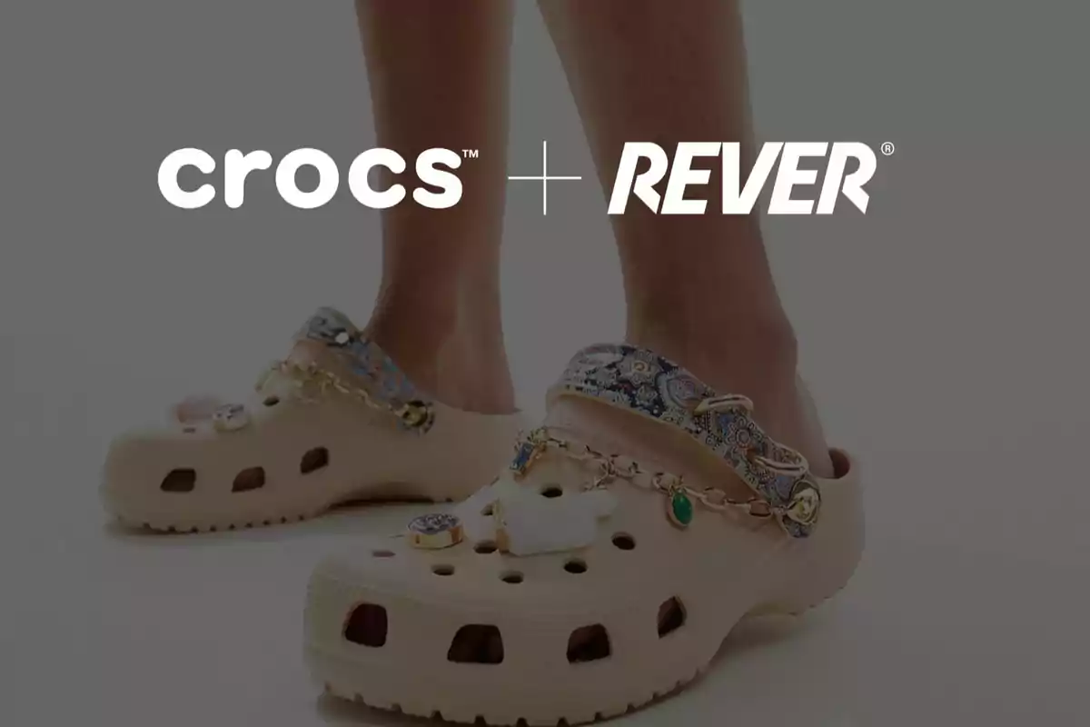 Persona usando Crocs beige decorados con accesorios y una correa estampada, con los logos de Crocs y Rever en la parte superior.