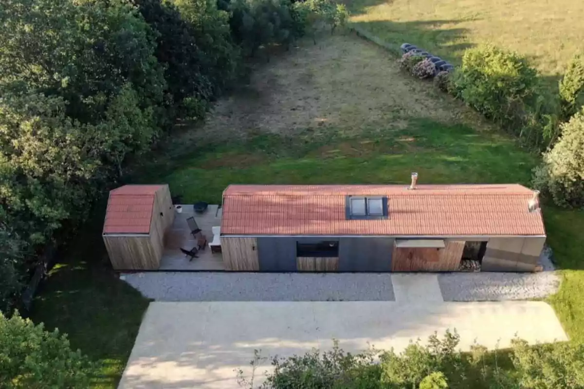 Casa moderna de una sola planta con techo de tejas rojas y terraza de madera rodeada de césped y árboles vista desde arriba