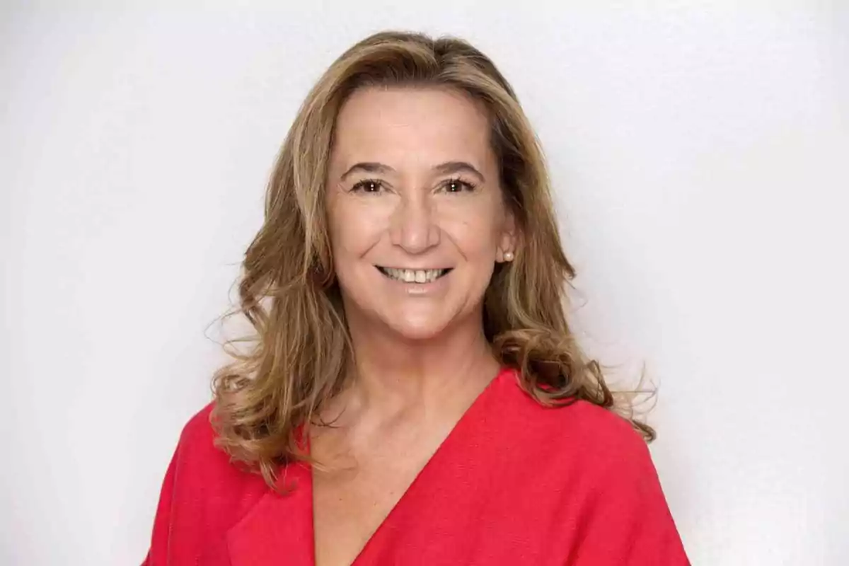 Mujer de cabello castaño claro y ondulado sonriendo y vistiendo una blusa roja frente a un fondo blanco