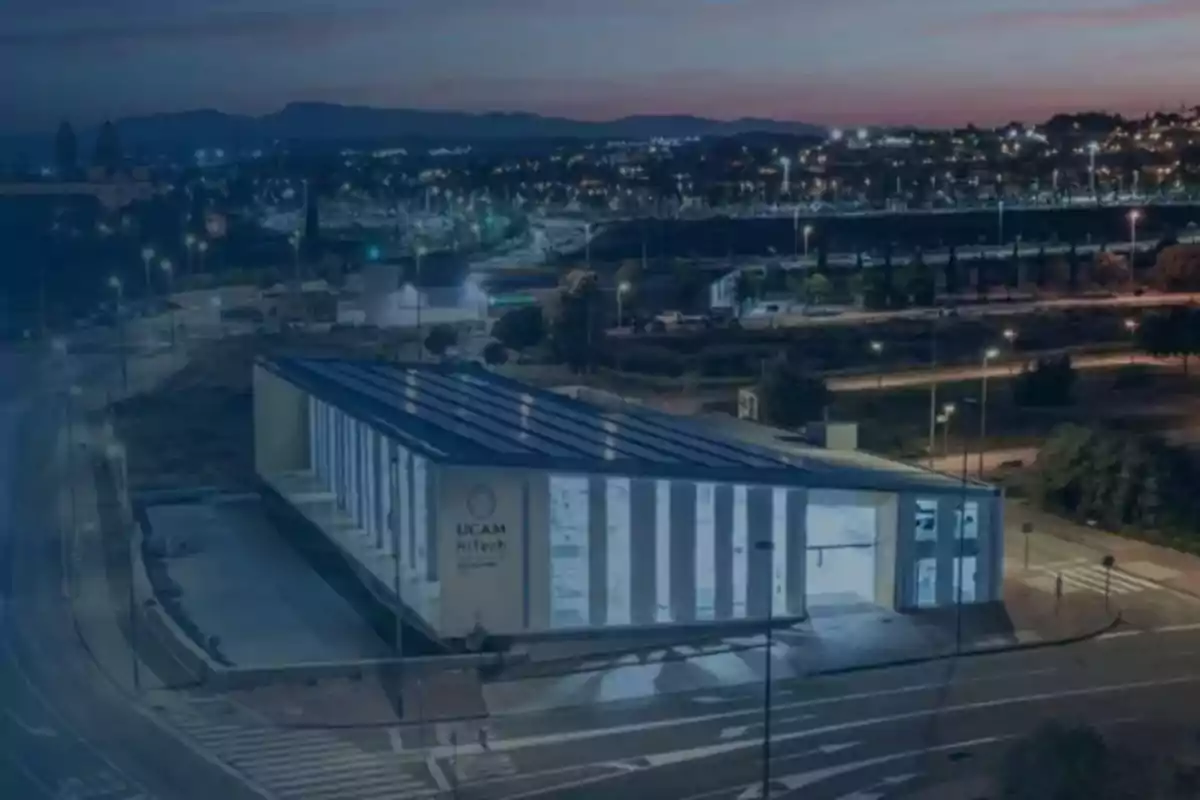 Vista nocturna de un edificio moderno con iluminación urbana y un paisaje de ciudad al fondo.