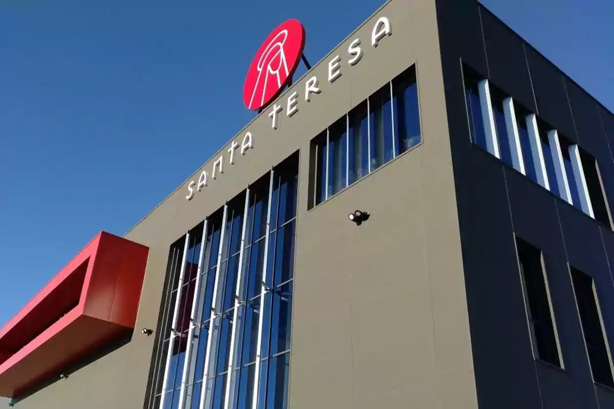 Edificio moderno con fachada gris y ventanas de vidrio reflejante, con un letrero que dice "Santa Teresa" y un logotipo rojo en la parte superior.