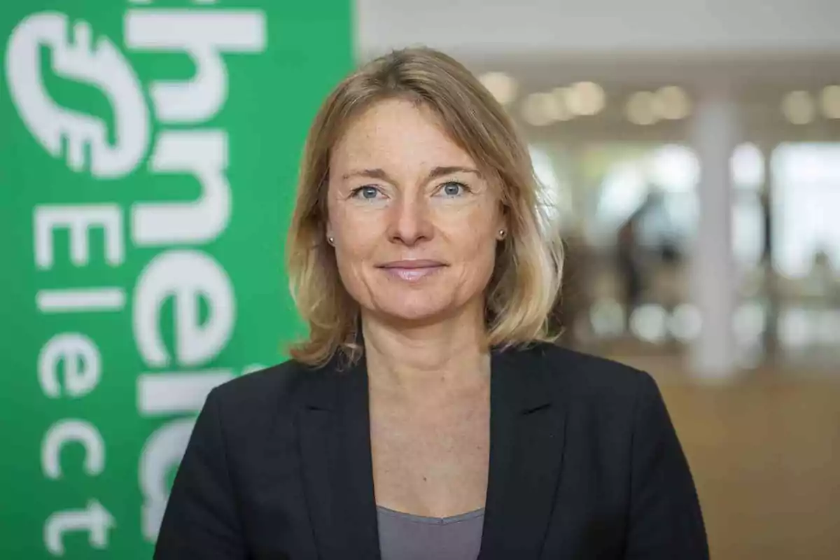 Una mujer de cabello rubio y chaqueta oscura frente a un fondo con el logo de Schneider Electric.