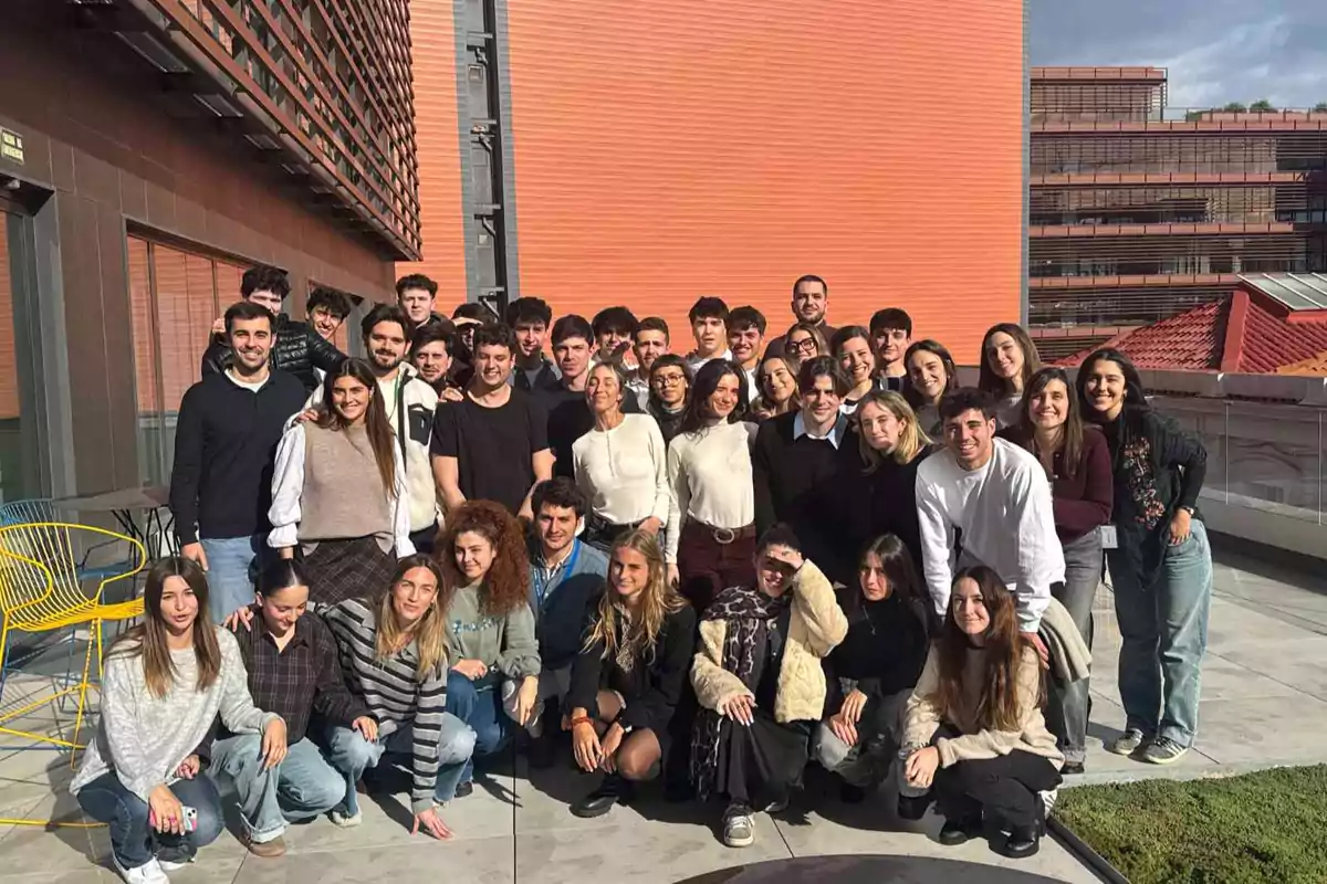 Grupo numeroso de jóvenes posando juntos al aire libre en una terraza con edificios modernos de fondo