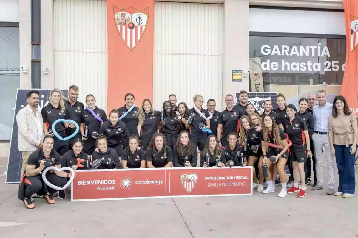 Un grupo de personas posando frente a un edificio con el escudo del Sevilla FC y un cartel que dice "Bienvenidos" y "Patrocinador Oficial Sevilla FC Femenino".