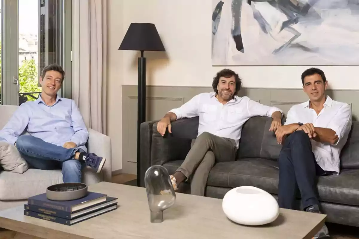 Tres hombres sentados en sofás en una sala de estar moderna con decoración minimalista.