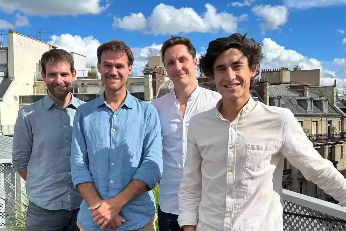 Cuatro personas posan sonriendo en una azotea con un cielo azul y nubes al fondo.