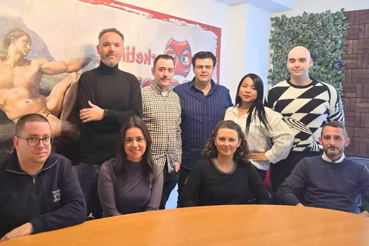 Un grupo de personas posando juntas en una sala de reuniones con una pintura clásica en la pared de fondo.