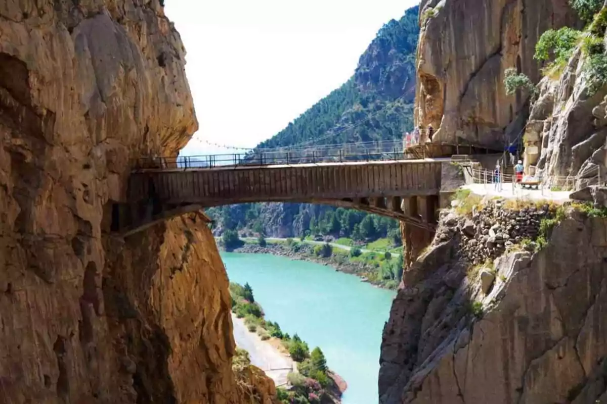 Puente de madera entre dos acantilados sobre un río de aguas turquesas rodeado de montañas y vegetación
