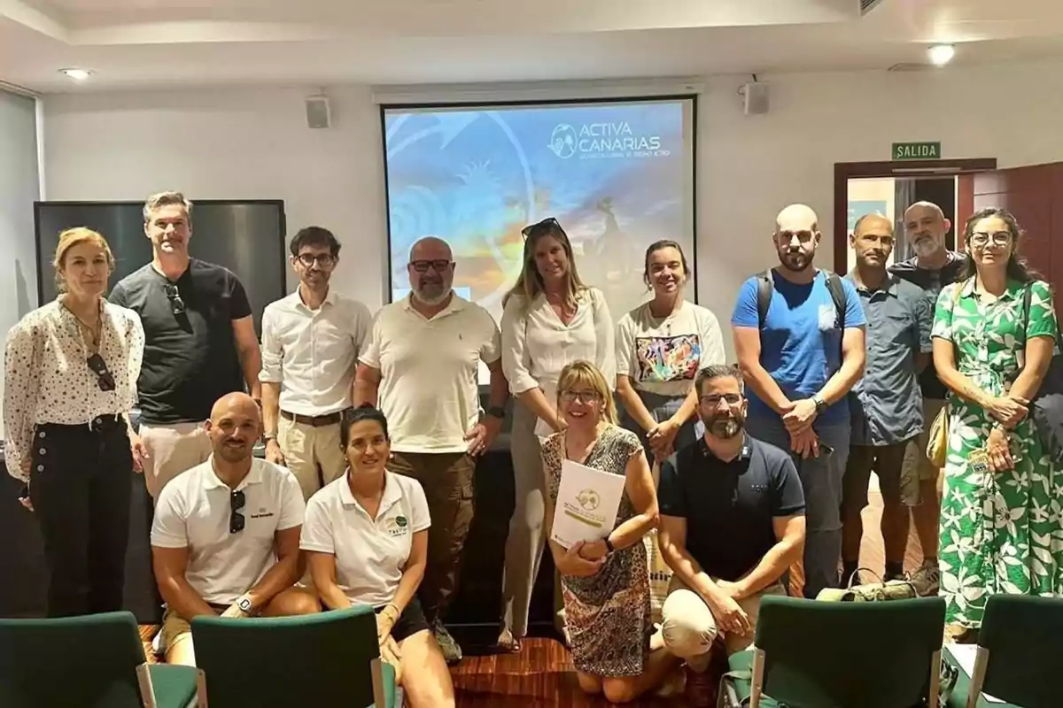 Un grupo de personas posando para una foto en una sala de conferencias con una pantalla de proyección al fondo que muestra el logo de "Activa Canarias".