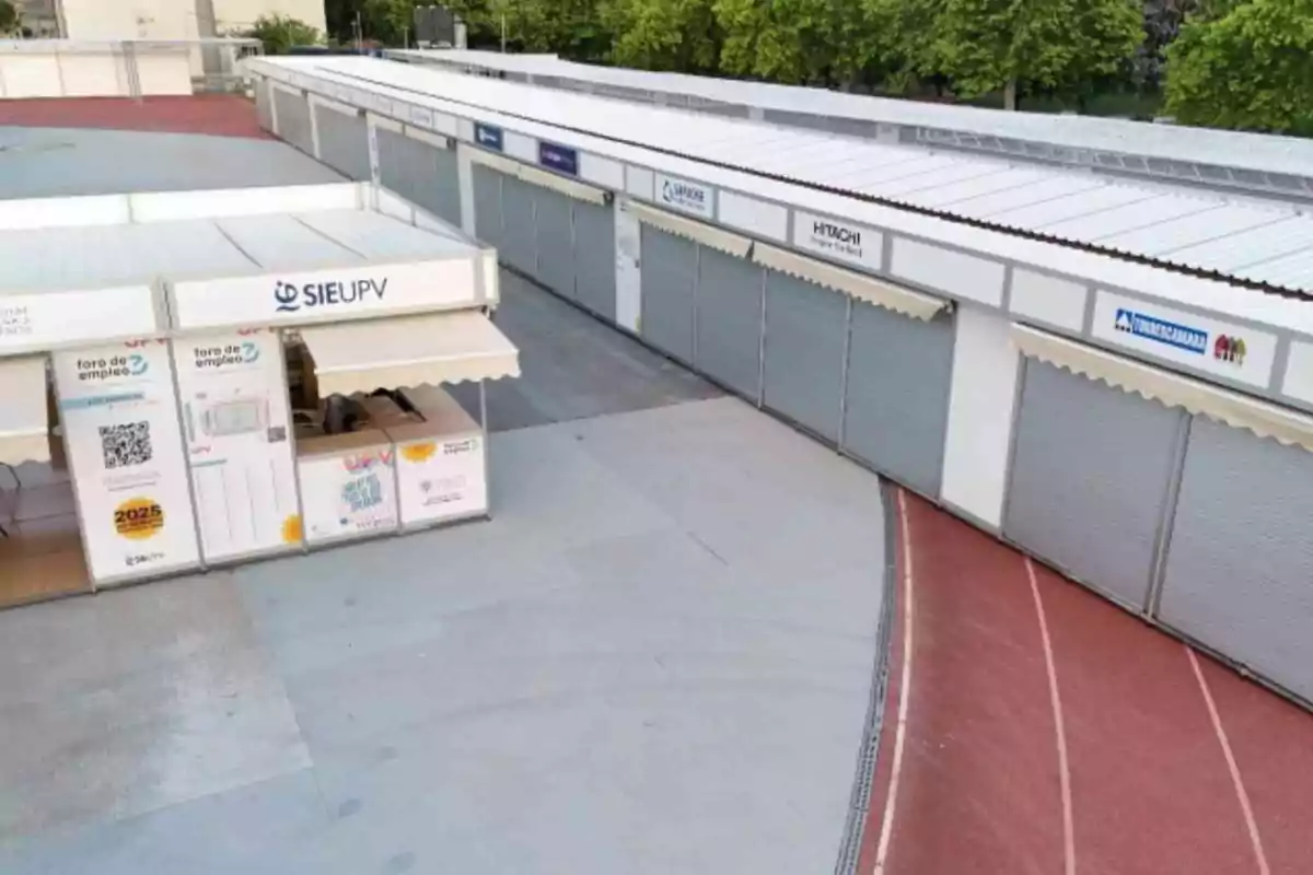 Vista de varios stands cerrados en una feria de empleo al aire libre con carteles de empresas y un módulo de información de la universidad