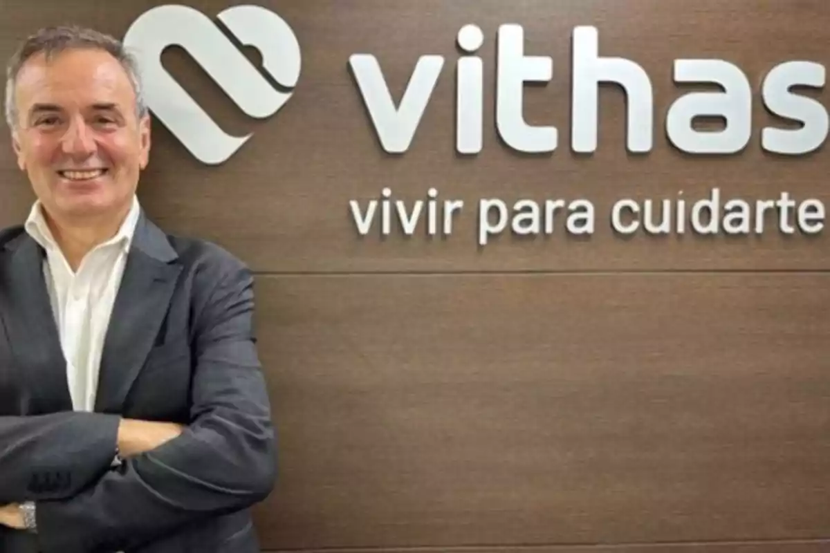 Hombre sonriendo con traje frente a un cartel de Vithas con el lema "vivir para cuidarte".