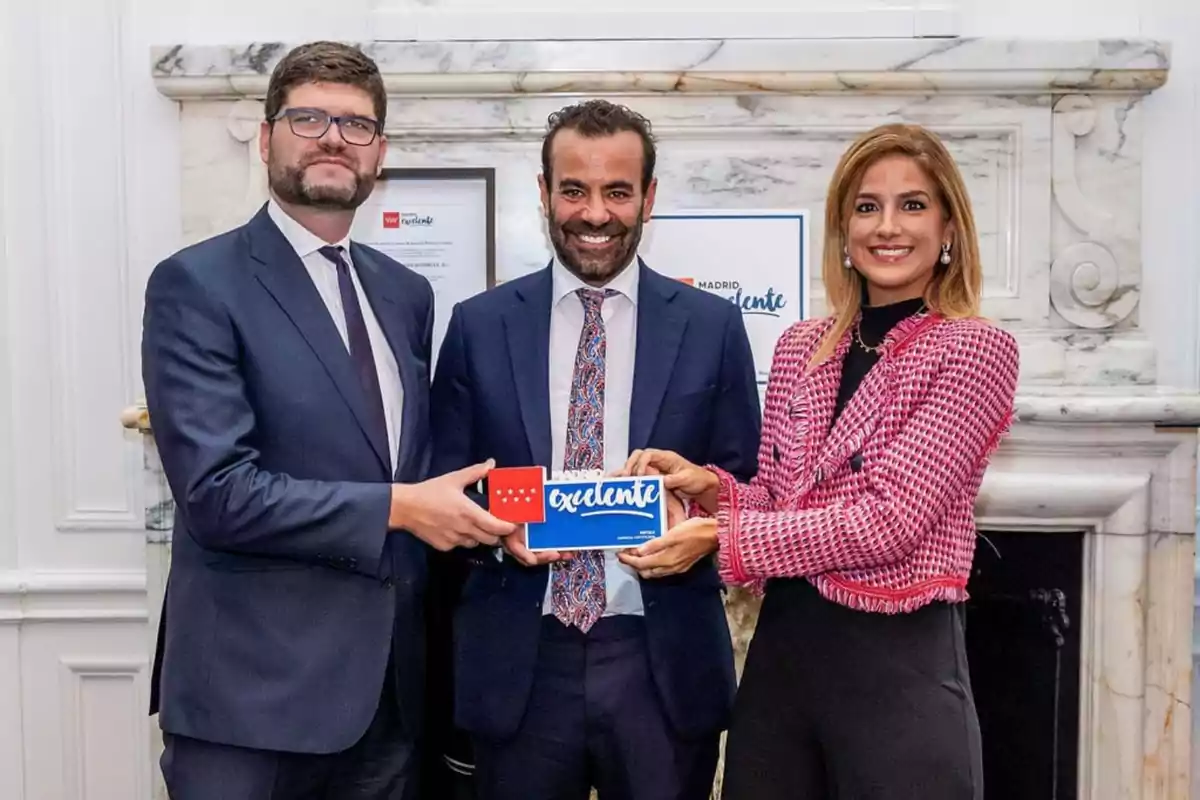 Tres personas posan sonrientes mientras sostienen un reconocimiento en un entorno formal.