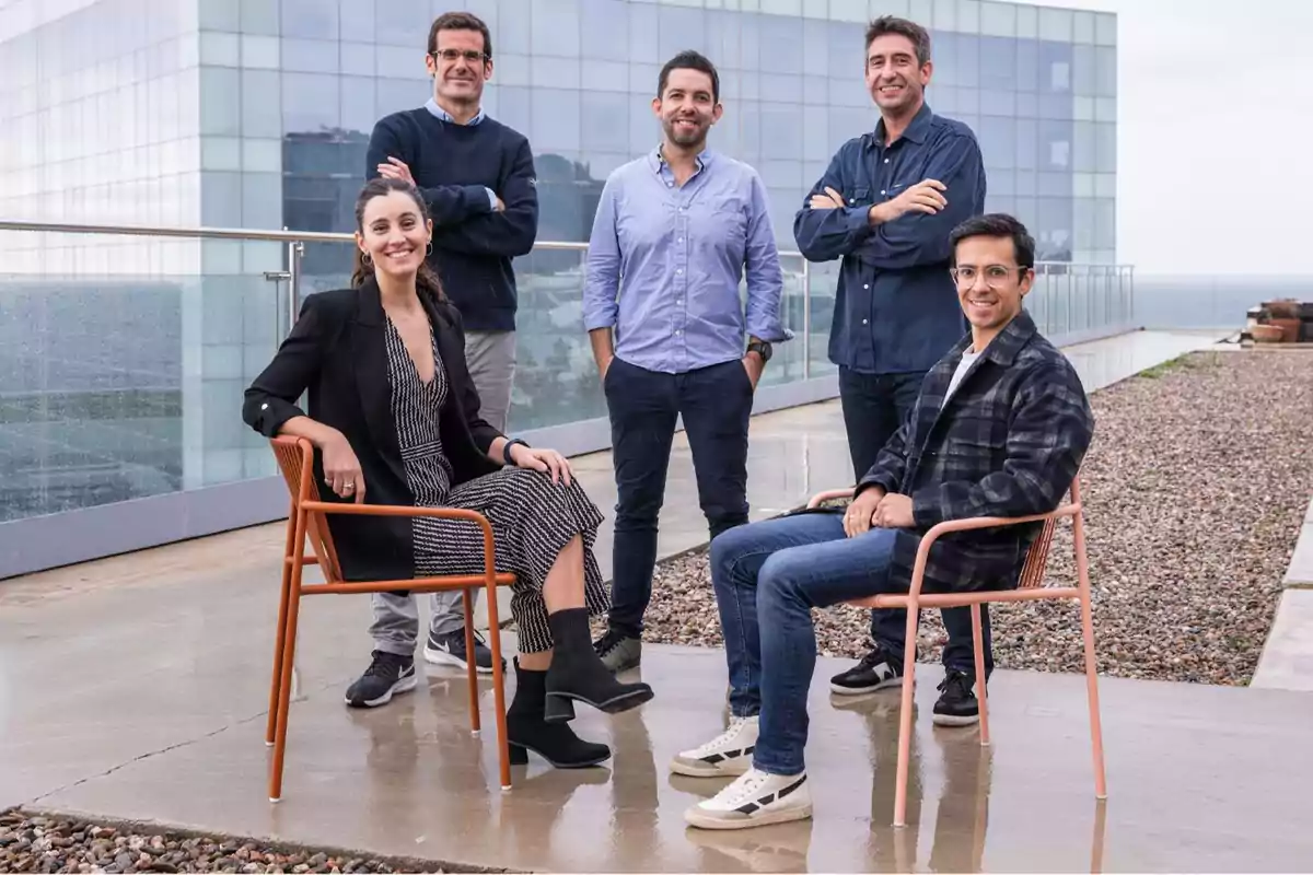 Cinco personas posan en una terraza con un edificio de fondo, dos están sentadas y tres de pie.