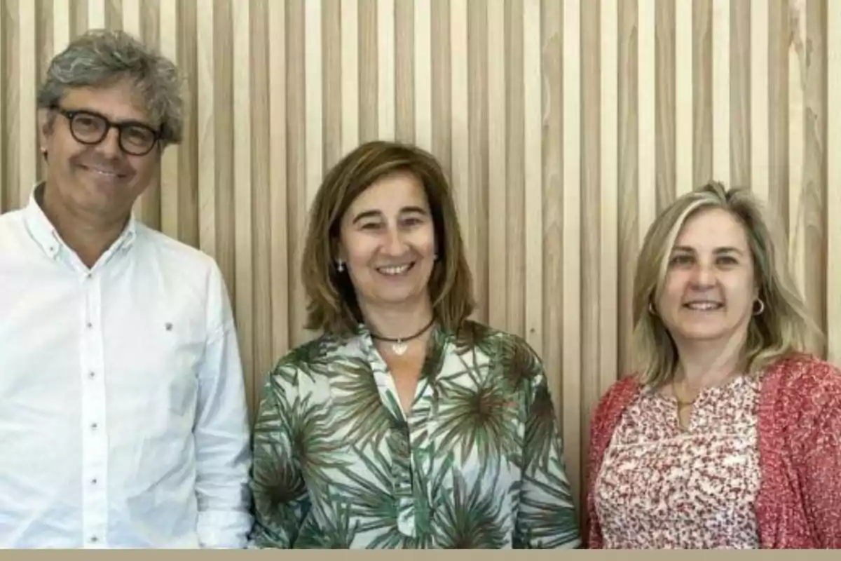 Tres personas posando frente a una pared de madera con listones verticales.