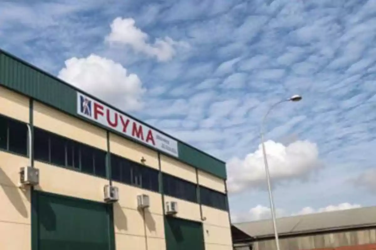 Edificio industrial con un cartel que dice "FUYMA" bajo un cielo parcialmente nublado.