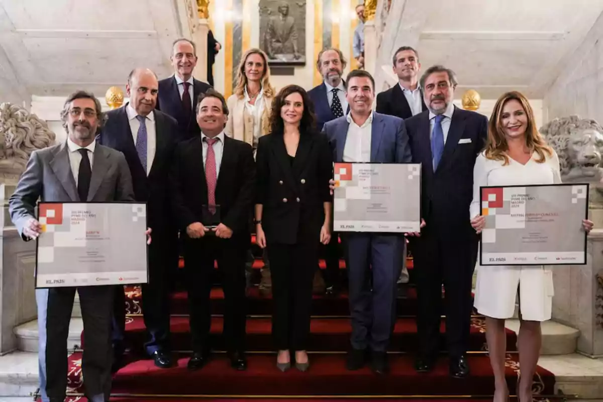 Un grupo de personas posando en una escalera elegante, algunas sosteniendo certificados.