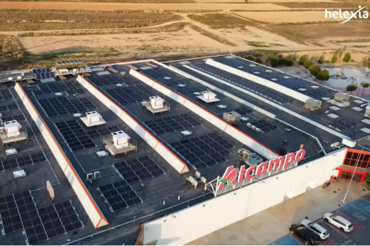 Vista aérea de un edificio con paneles solares en el techo y un letrero de "Alcampo" en la fachada.