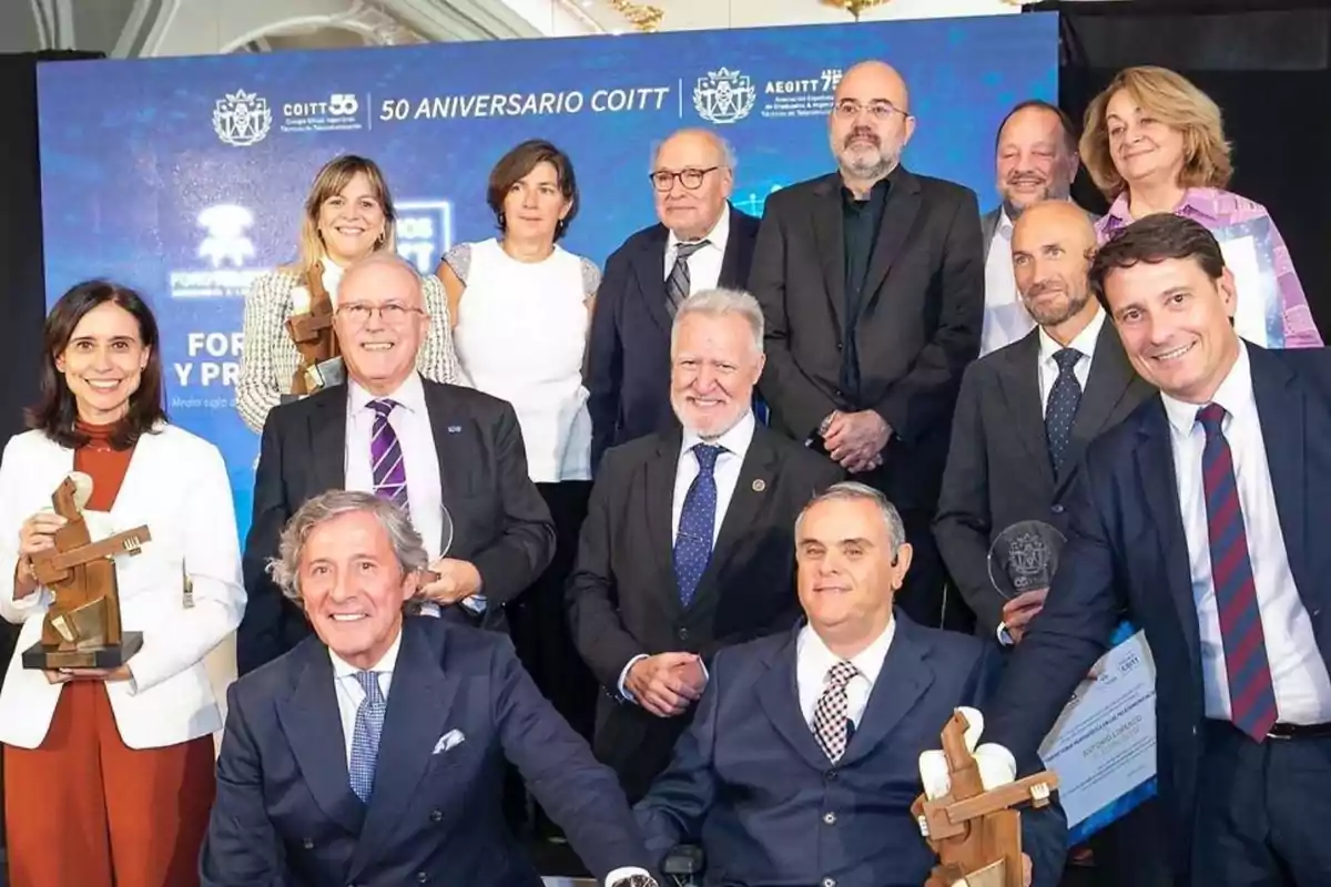 Un grupo de personas posando con trofeos y certificados en un evento de celebración del 50 aniversario del COITT, con un fondo azul que muestra el logotipo del evento.