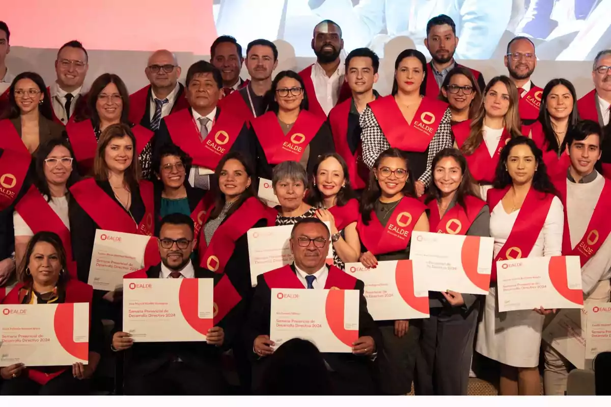 Un grupo de personas sonrientes posando con diplomas y vestidas con bandas rojas de graduación.