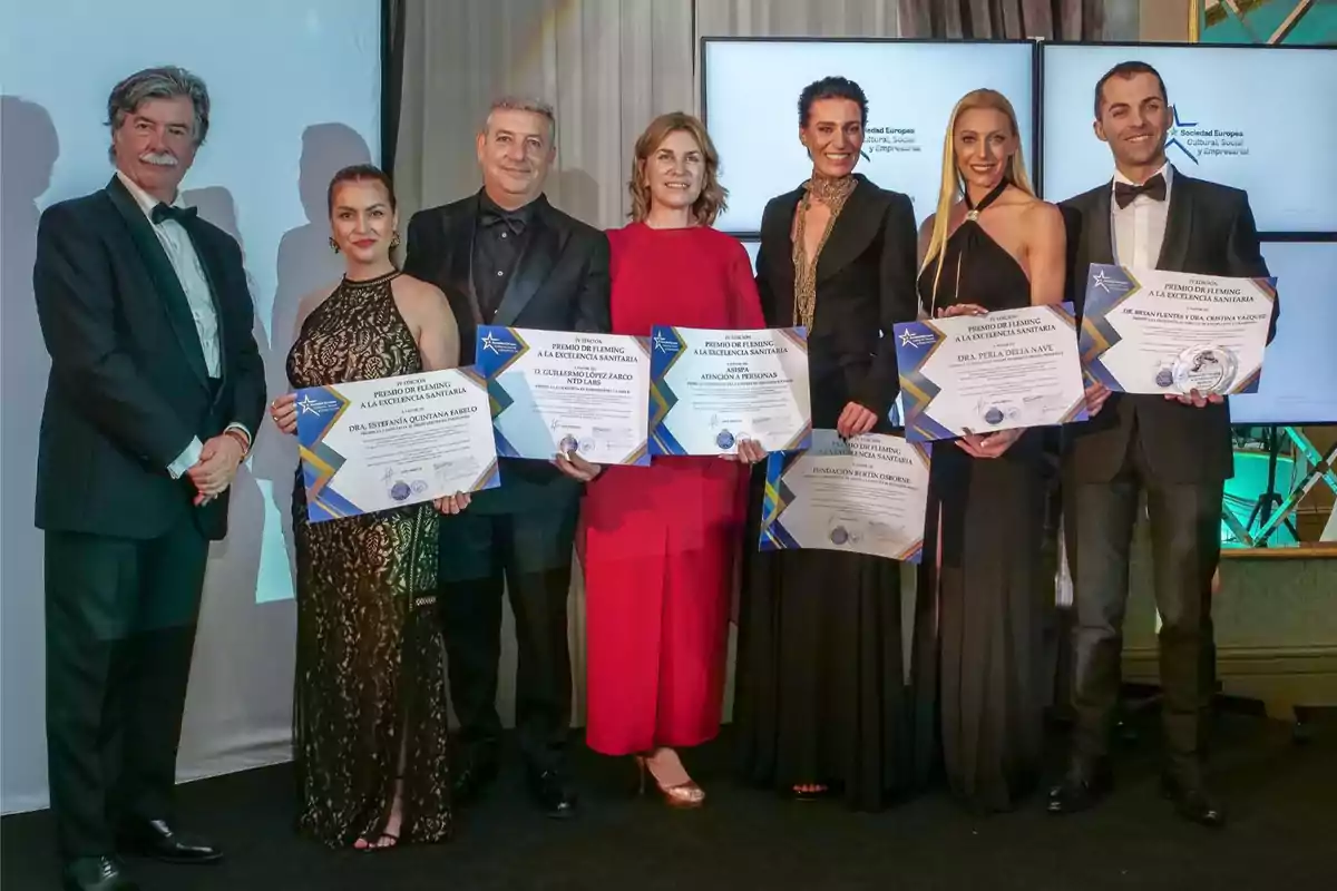 Un grupo de personas vestidas de gala sostiene certificados en un evento de premiación.