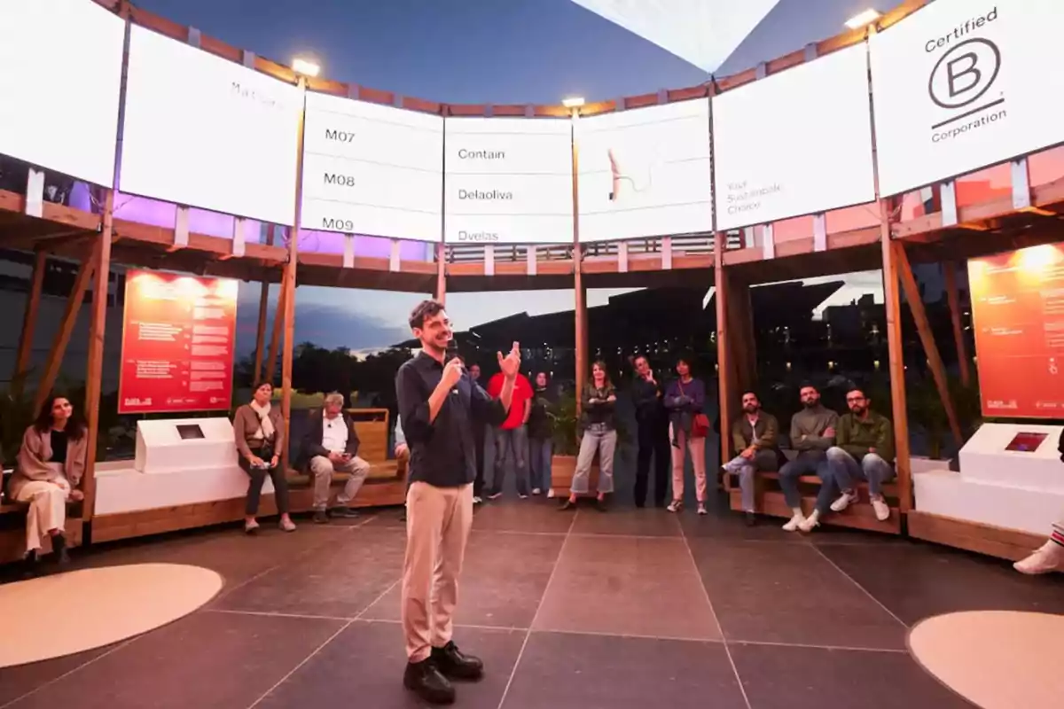 Un grupo de personas escucha atentamente a un orador en un espacio moderno con pantallas iluminadas y un ambiente acogedor.