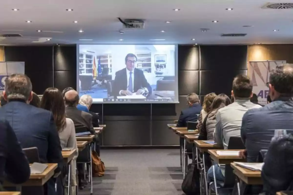 Personas sentadas en un salón de conferencias viendo una presentación en pantalla grande.