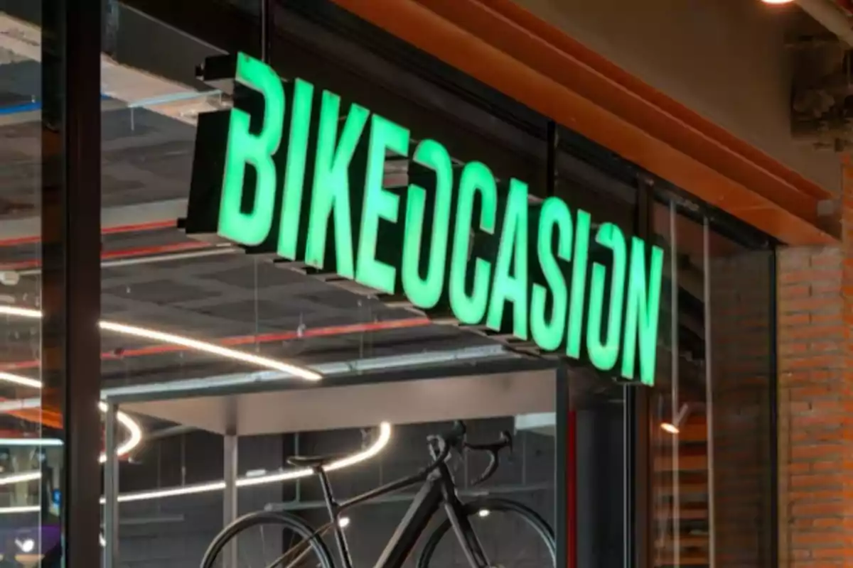 Letrero verde de una tienda de bicicletas llamado "Bikeocasion" con una bicicleta en exhibición en el interior.