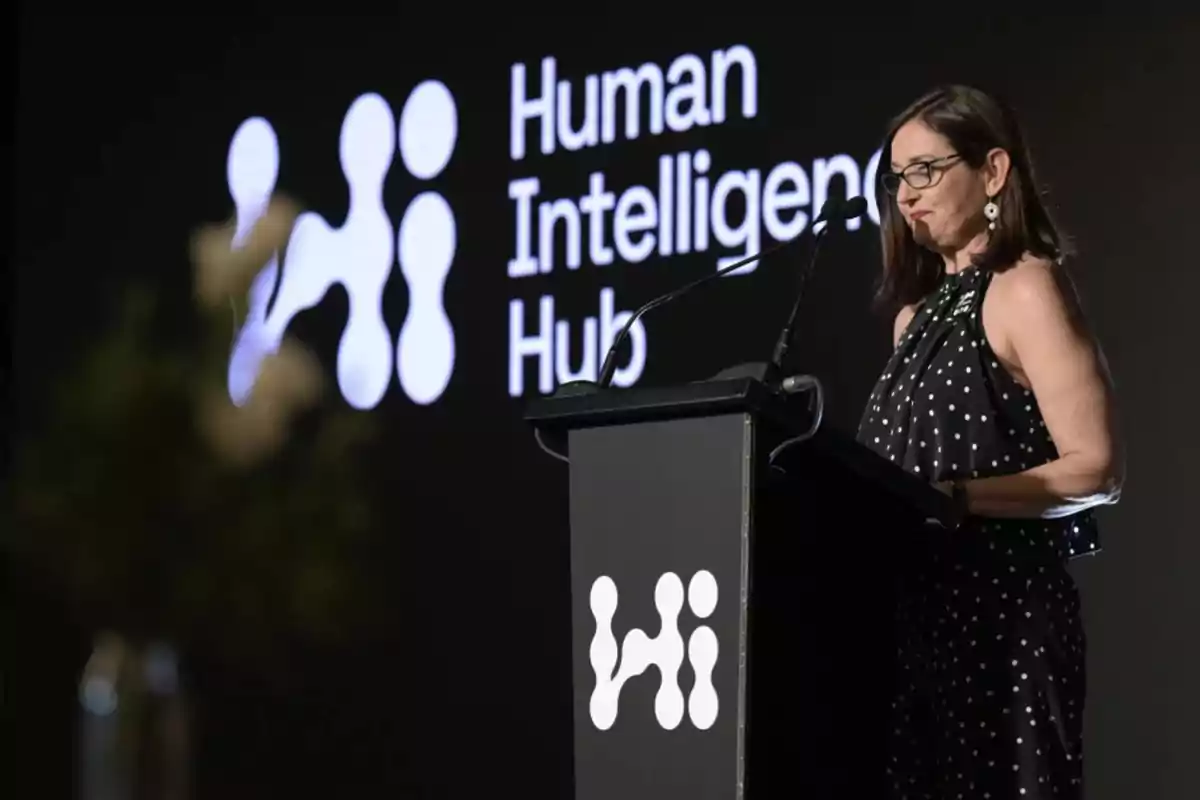 Mujer hablando en un podio con el logo de Human Intelligence Hub en el fondo.