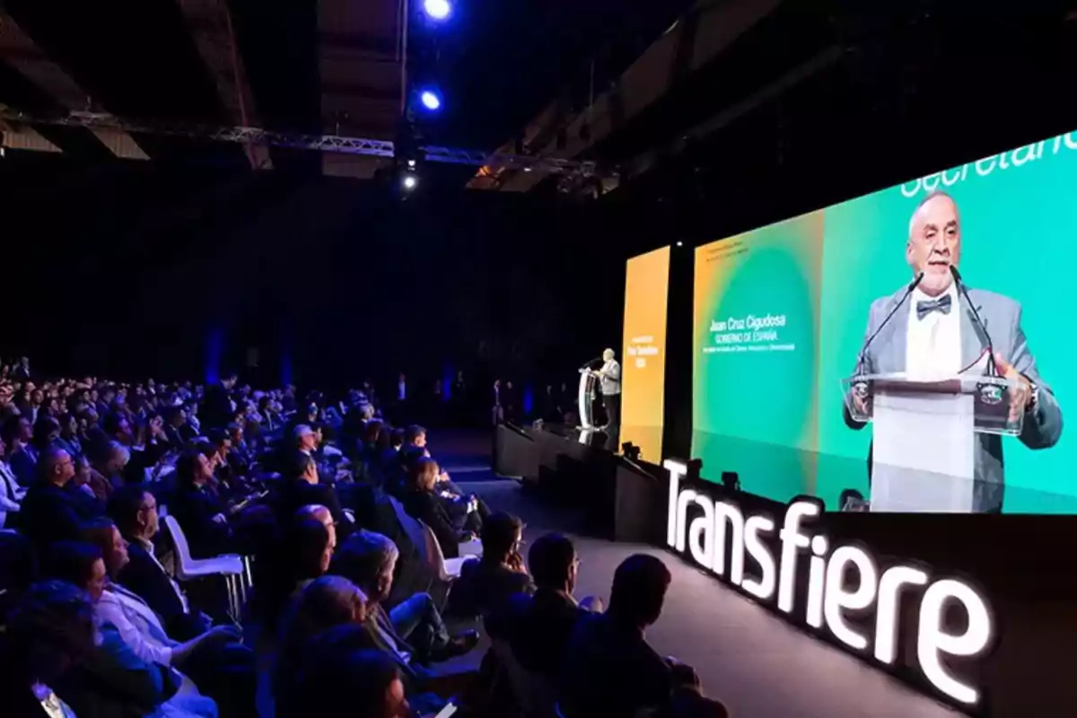 Una persona hablando en un escenario durante un evento llamado Transfiere con una audiencia sentada frente a él.