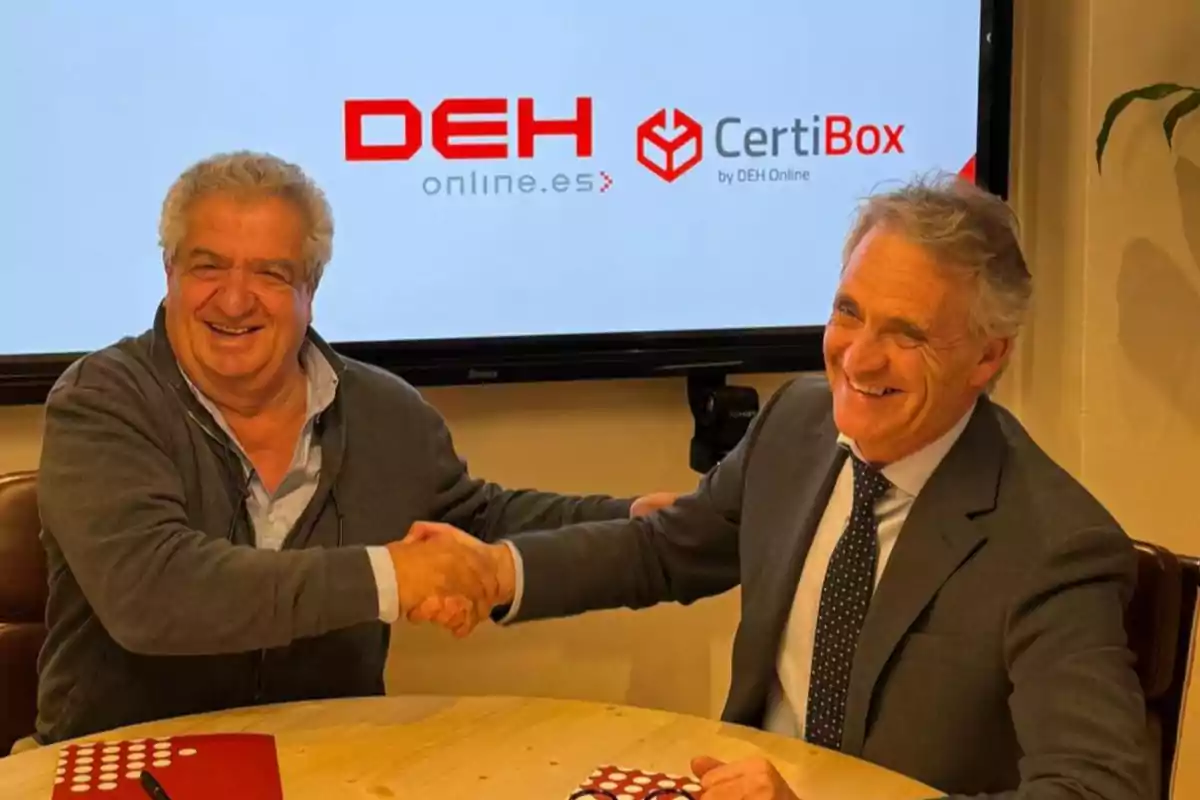 Dos hombres sonrientes se dan la mano en una reunión de negocios frente a una pantalla que muestra los logotipos de DEH Online y CertiBox.