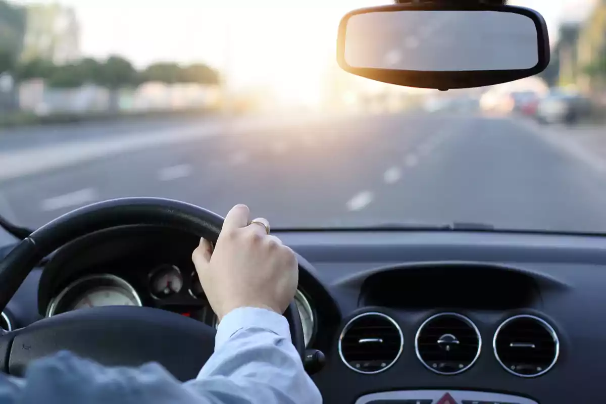 Persona conduciendo un automóvil en una carretera despejada al atardecer.