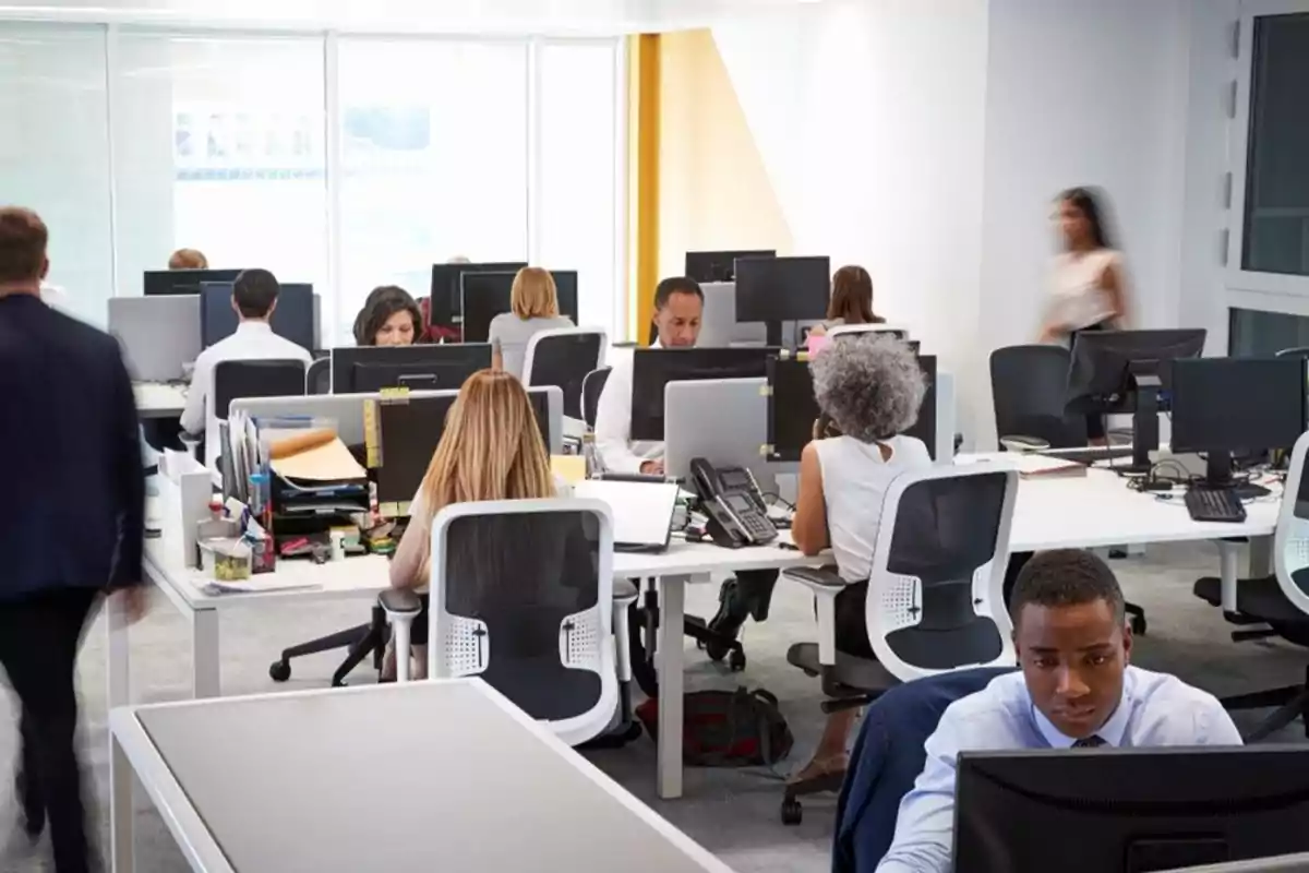 Personas trabajando en una oficina moderna con escritorios compartidos y computadoras