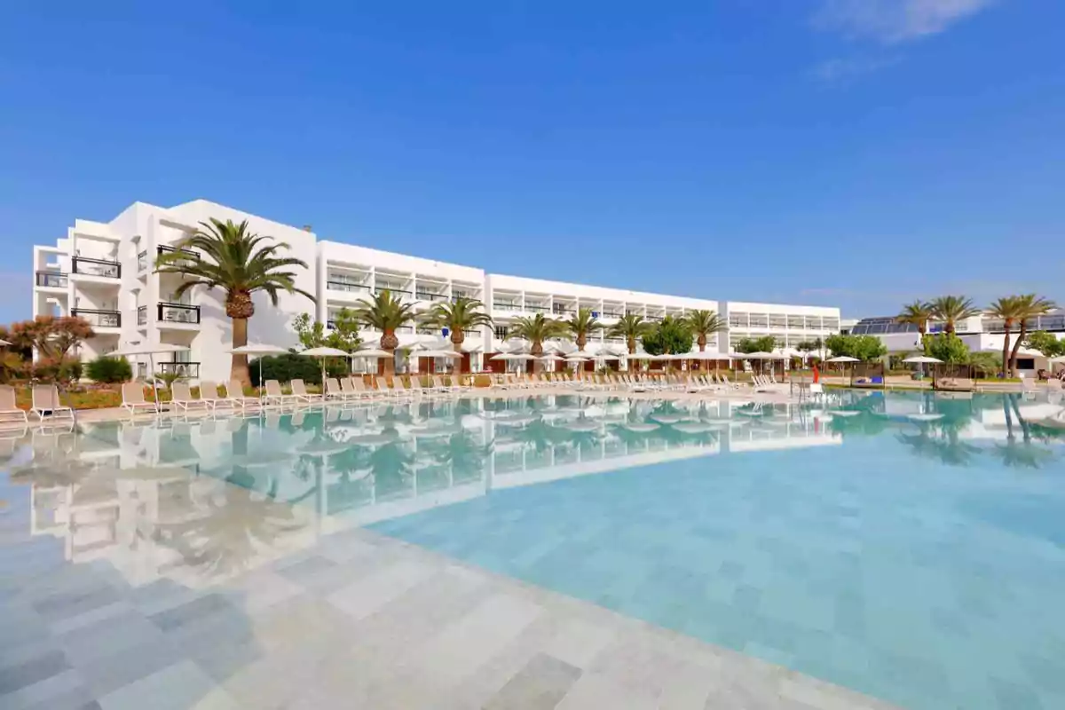 Edificio moderno con piscina y palmeras bajo un cielo despejado.