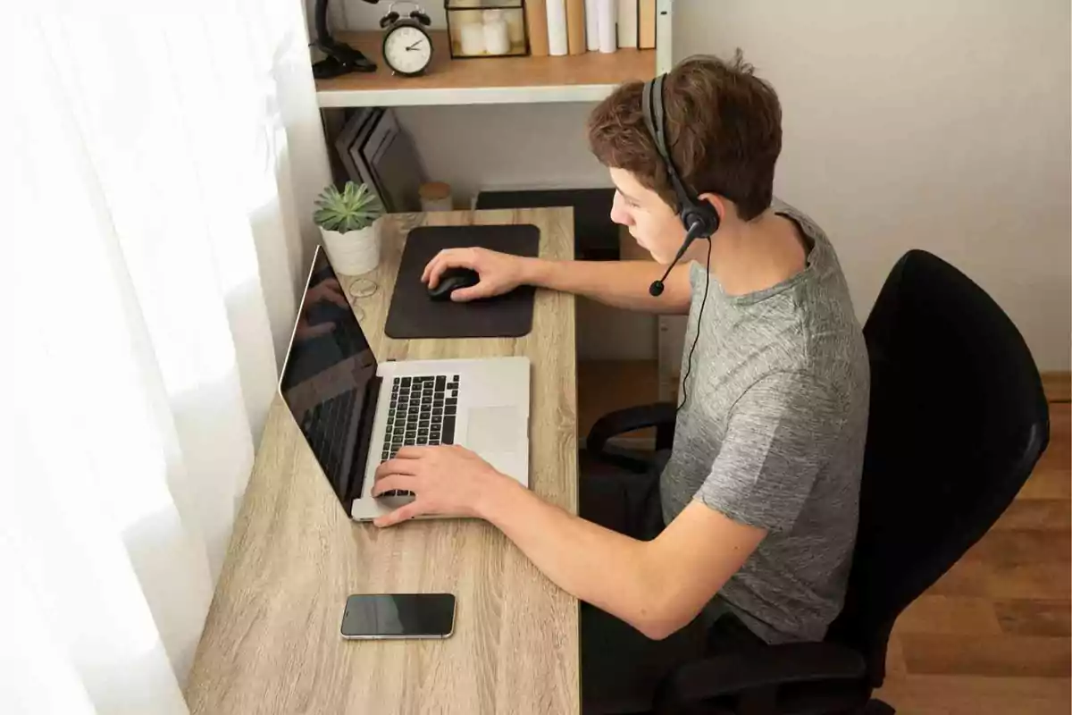 Persona trabajando en una computadora portátil con auriculares en un escritorio ordenado.